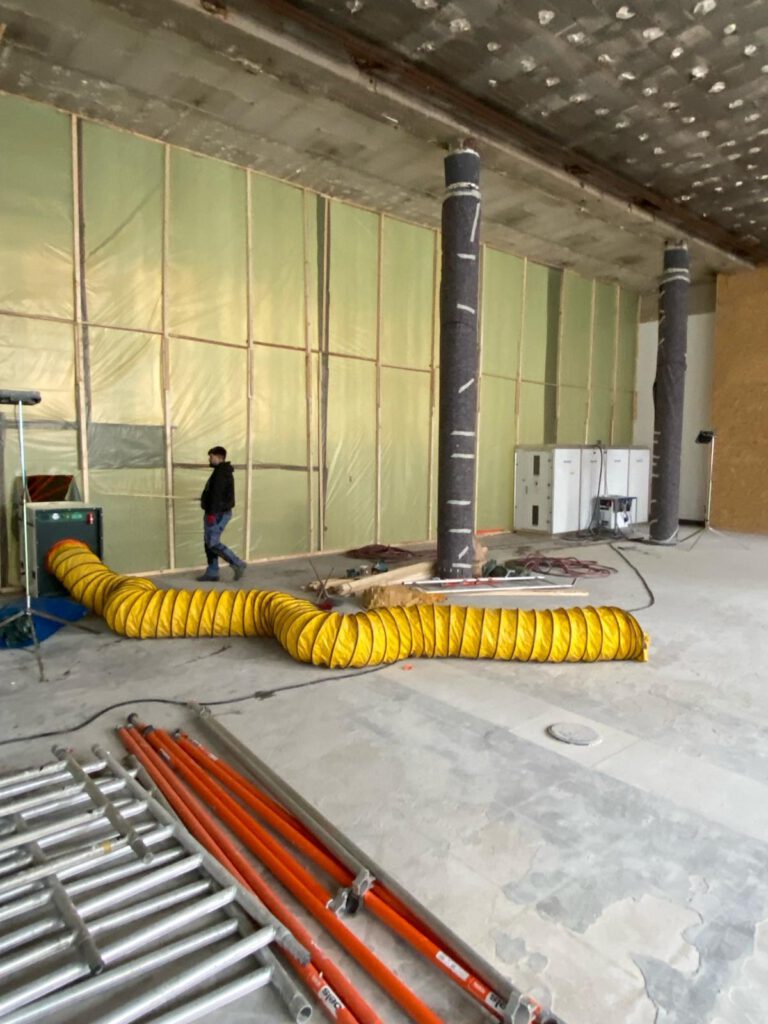 Großer Innenraum mit Folienwand, ummantelten Stützen und gelbem Lüftungsschlauch.