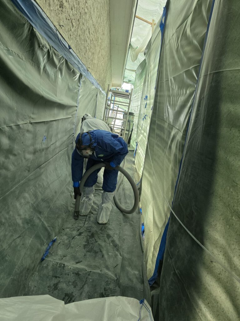 Person in Schutzanzug bei Asbestsanierung in einem abgedeckten Arbeitsbereich
