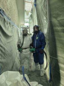 Zwei Personen in Schutzanzügen und Atemschutz bei der Asbestsanierung