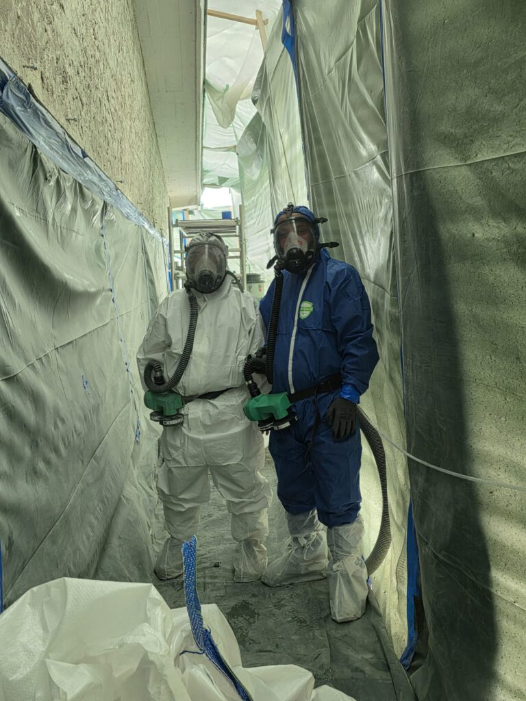 Zwei Personen in Schutzanzügen und Atemschutz bei der Asbestsanierung