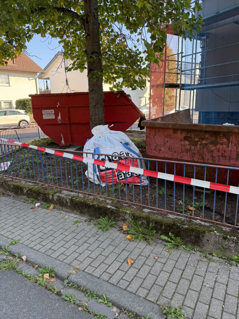 Großer weißer Asbestentsorgungssack neben Containern mit Absperrband