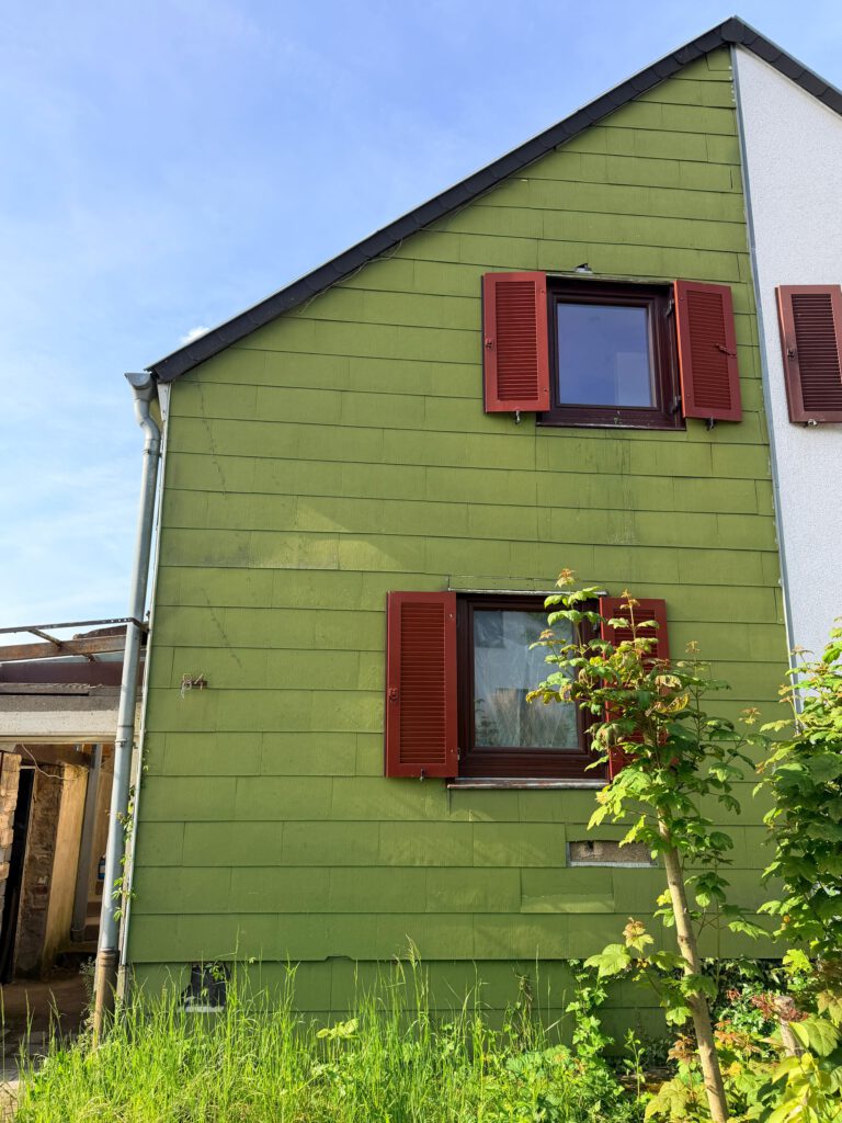 Hausfassade mit grüner Verkleidung und roten Fensterläden