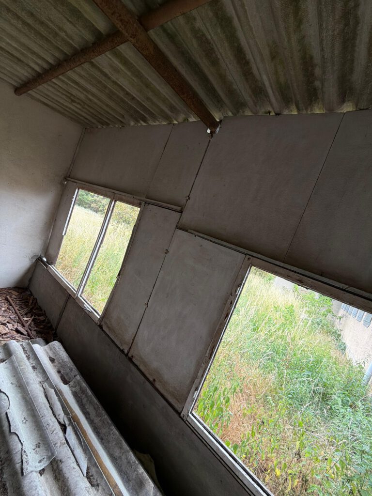 Verlassener Raum mit asbesthaltigen Wellplatten und offenen Fenstern