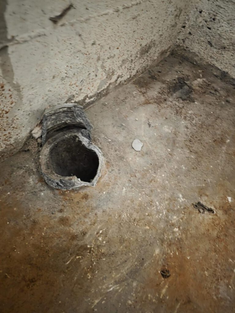 beschädigter Asbestboden mit offenem Rohr im Raumwinkel