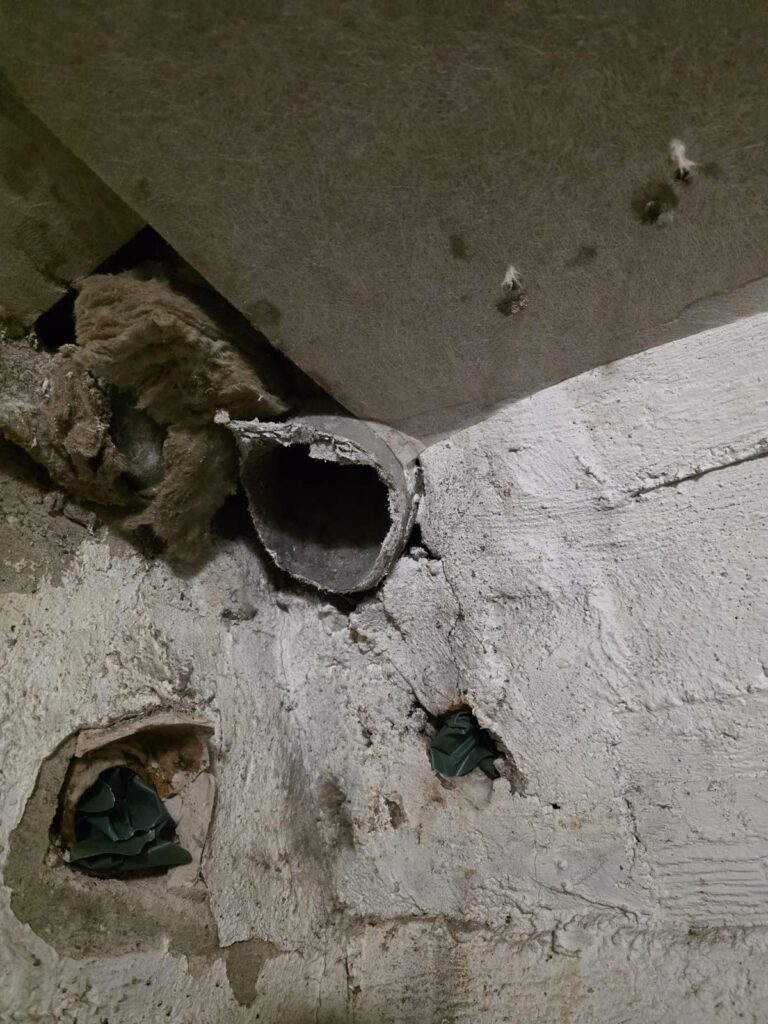 Beschädigte Asbestplatte mit Öffnungen und Rohr in Decke