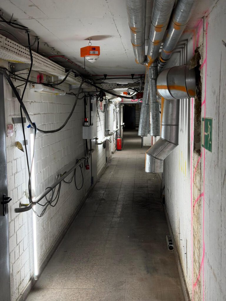 Asbestentsorgung – Dunkler Flur mit Lüftungsrohren und elektrischen Leitungen