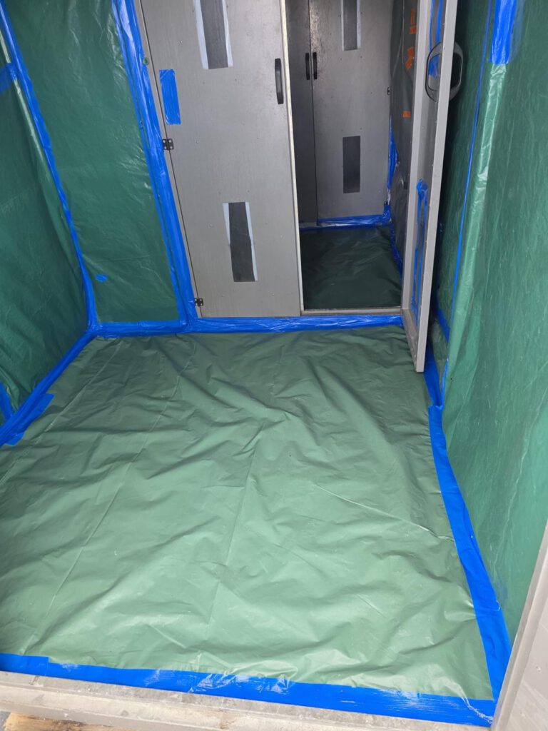 Arbeitsbereich mit grünem Schutzvlies und blauem Klebeband bei Asbestsanierung