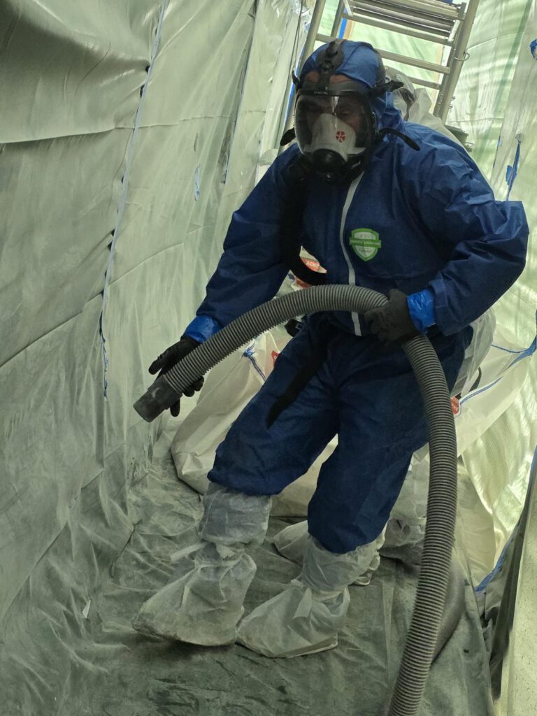 Arbeiter im Schutzanzug bei der Asbestsanierung mit Schlauch